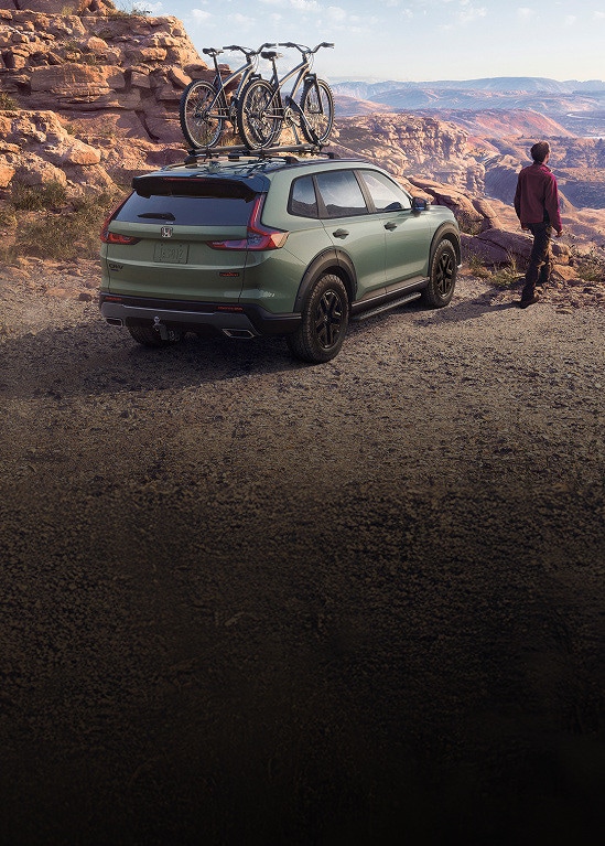 2026 Honda CR-V TrailSport Hybrid in Ash Green Metallic parked on a rocky canyon with bikes on roof (Compact Crossover SUV).