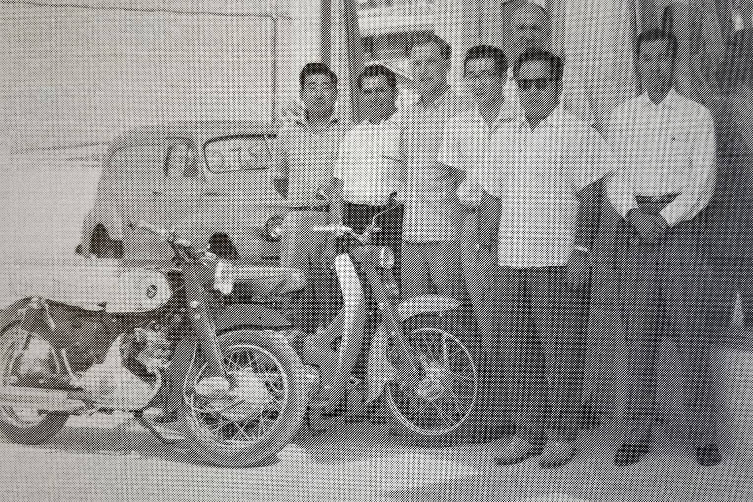 Honda employees posing for a photo with classic Honda motorcycles.